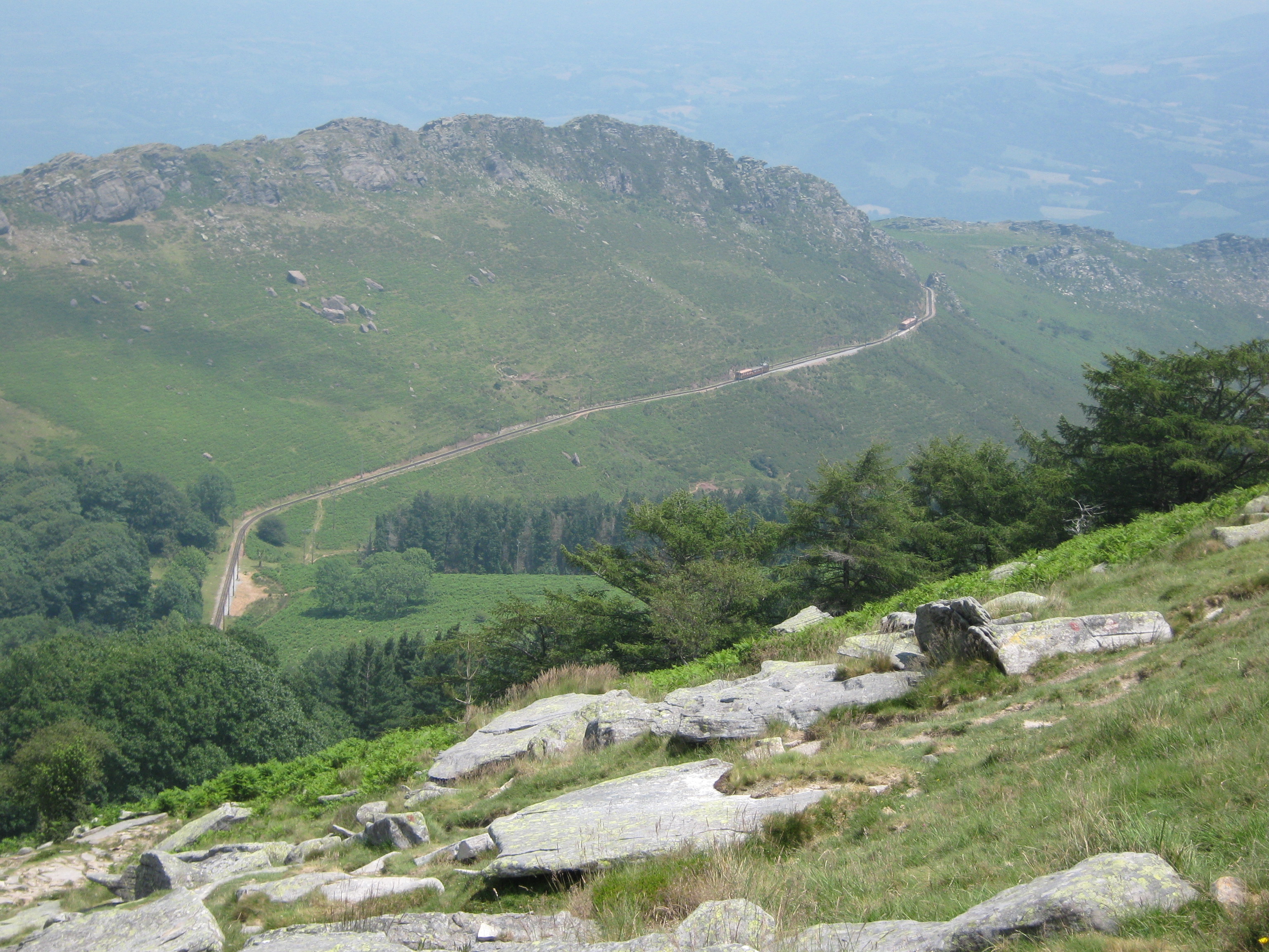 Two trains of the Chemin de Fer de la Rhune climbing through the Basque mountain landscape near the summit.