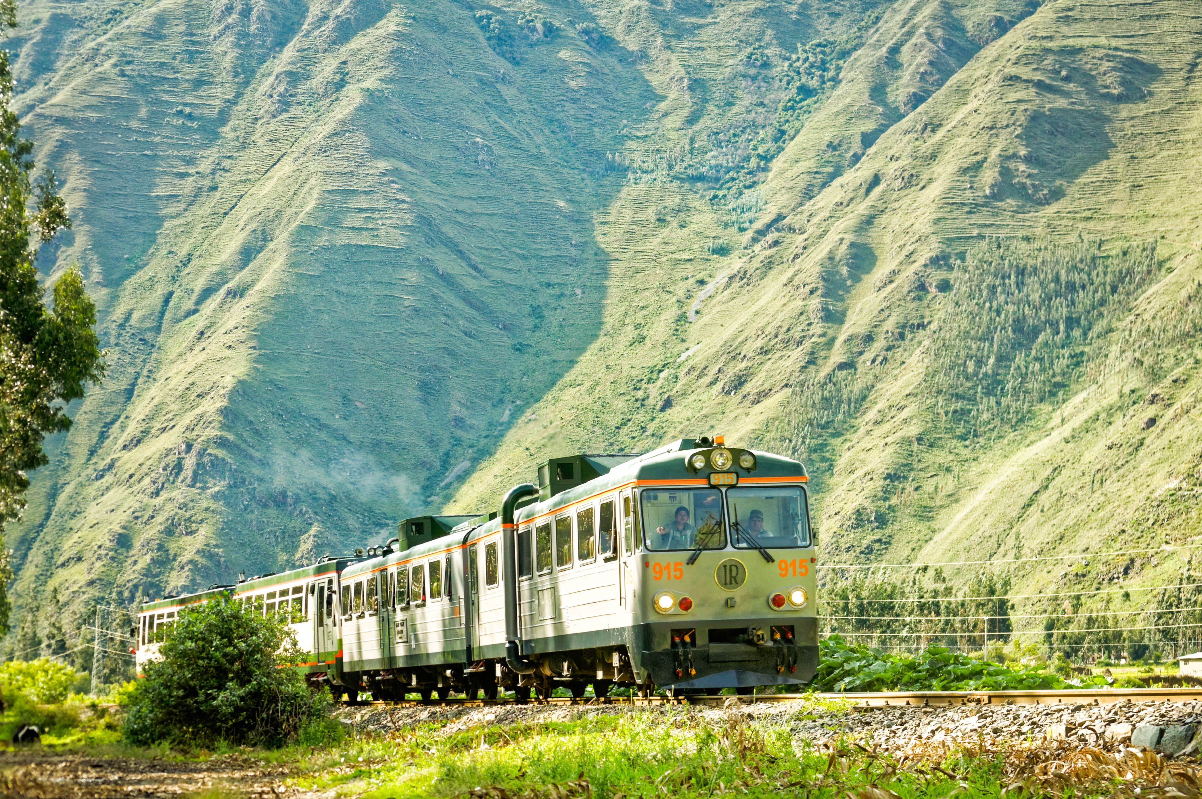 An Inca Rail train running below steep green Andean hillsides on the line towards Machu Picchu.