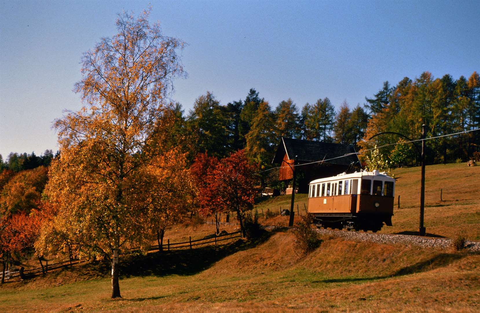 Heritage Ritten Railway railcar crossing autumnal South Tyrol countryside.