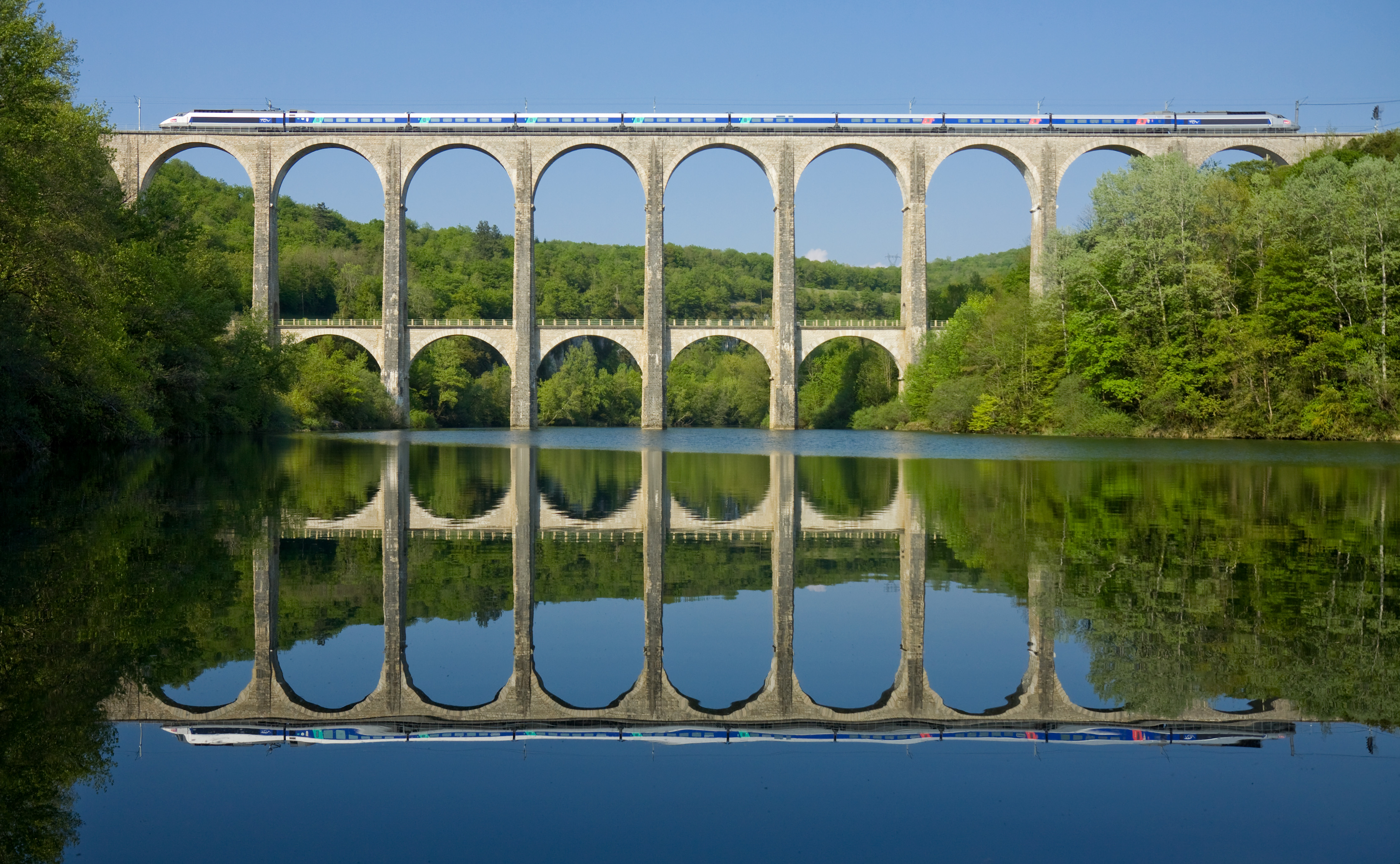 An SNCF TGV crosses the Cize-Bolozon viaduct over open French countryside.