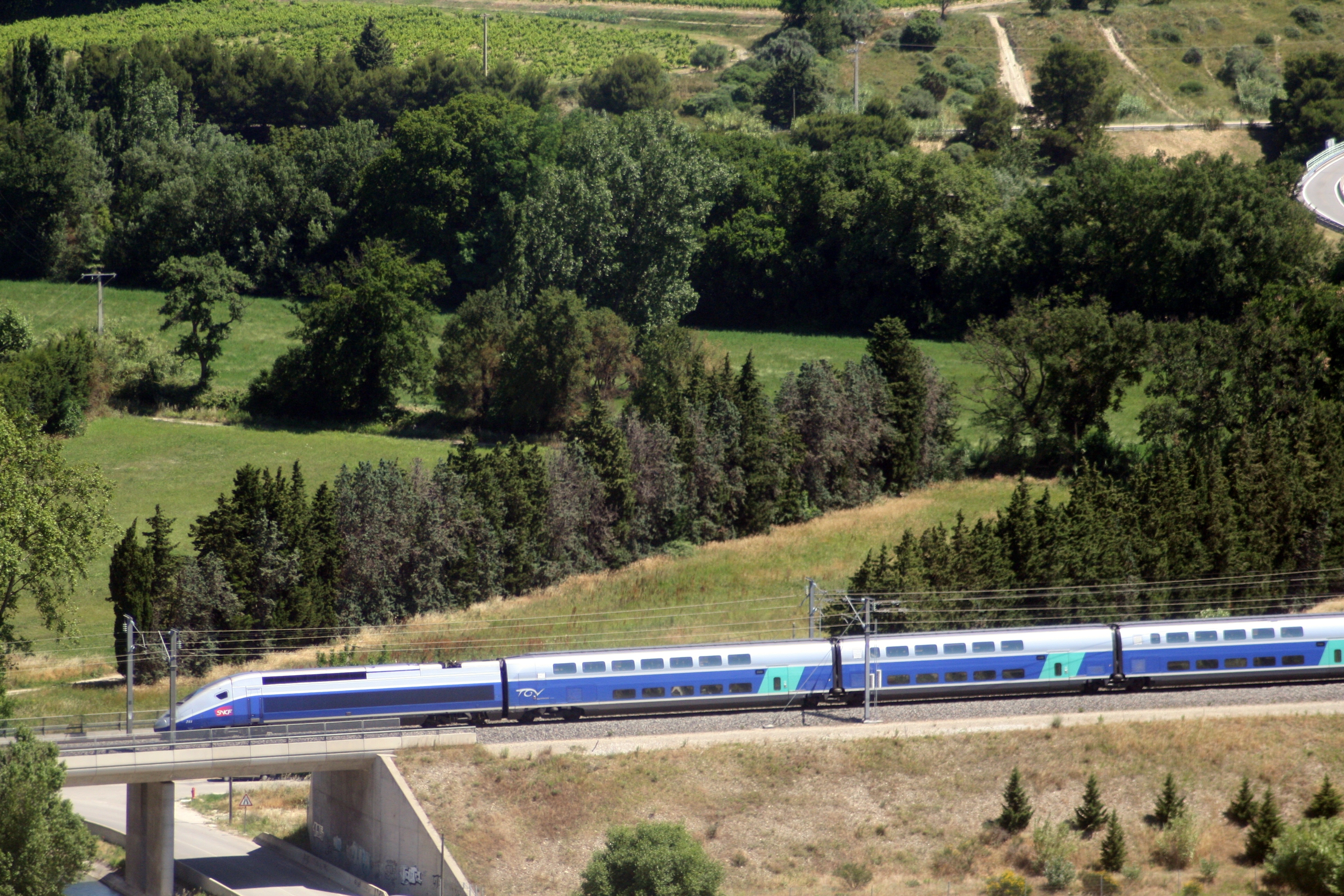 A TGV Duplex runs at speed across the sunlit Provencal landscape on the LGV Mediterranee.