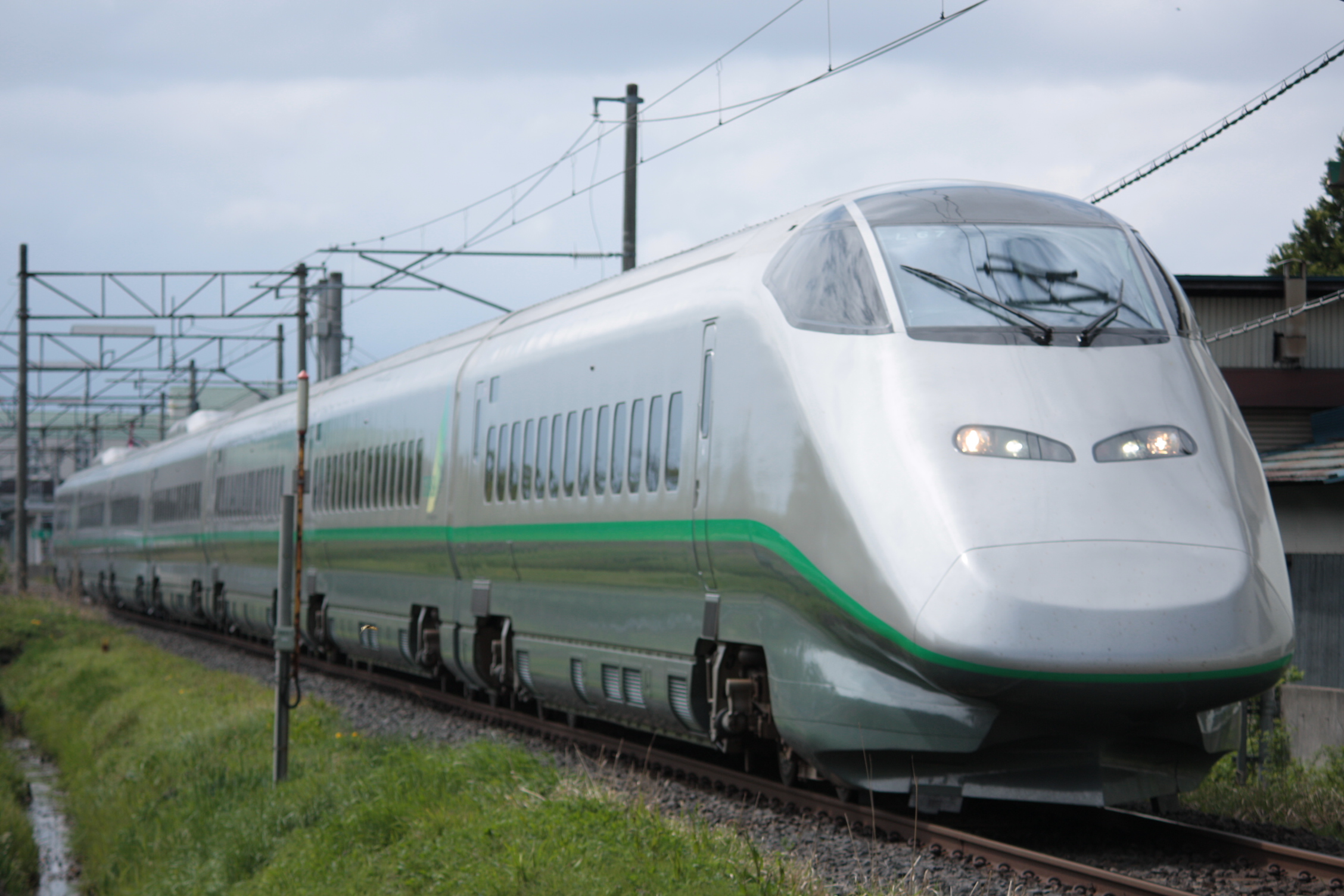 An E3 series Tsubasa train of the Yamagata Shinkansen runs through open countryside.