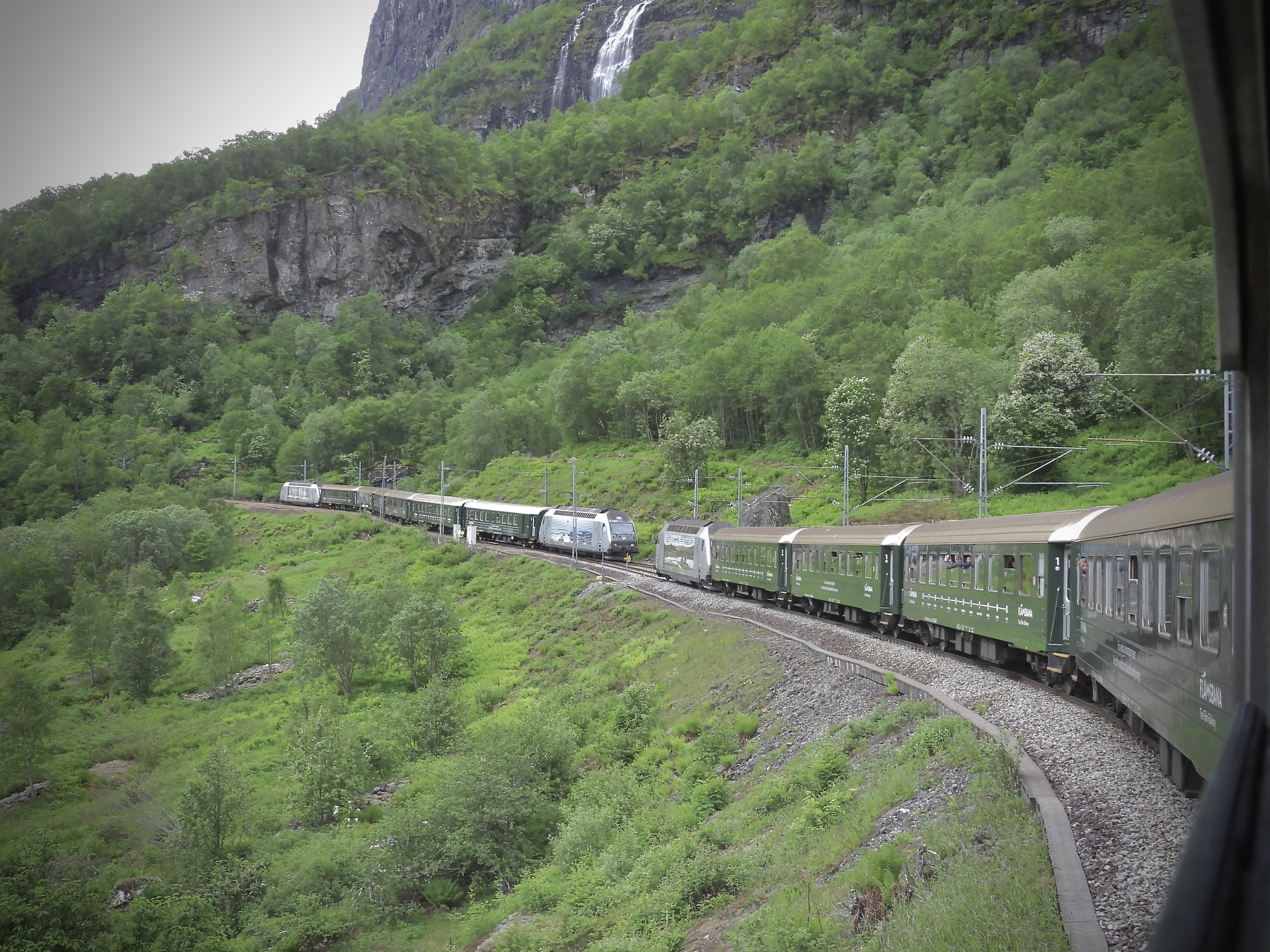 Two Flåm Railway trains passing beneath Brekkefossen waterfall.