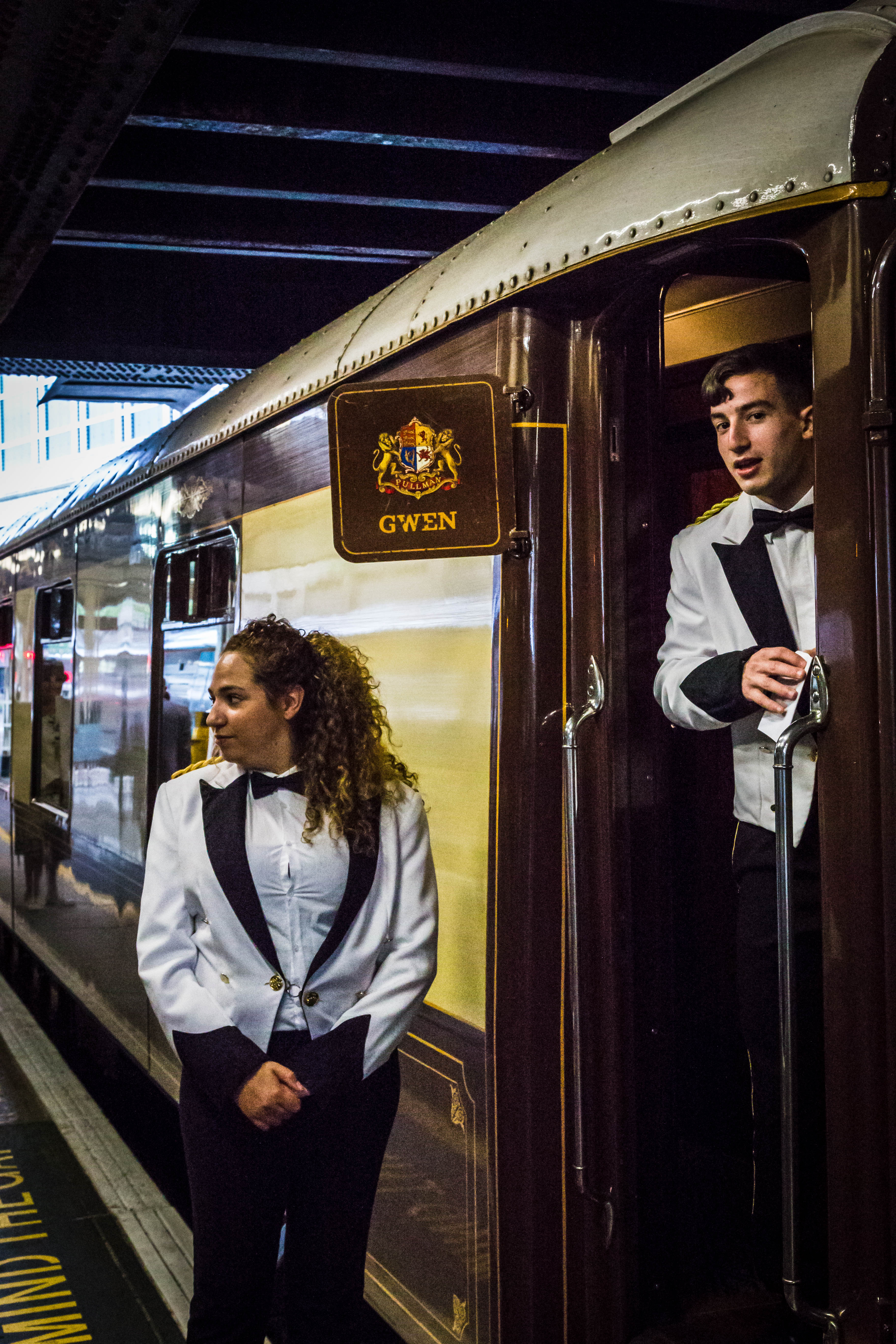 British Pullman stewards in white jackets beside Pullman car Gwen at London Victoria.