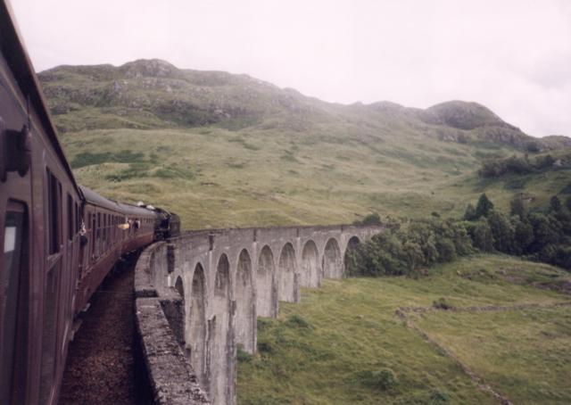The Jacobite steam train crosses the 21-arch Glenfinnan Viaduct with the Highland landscape behind.