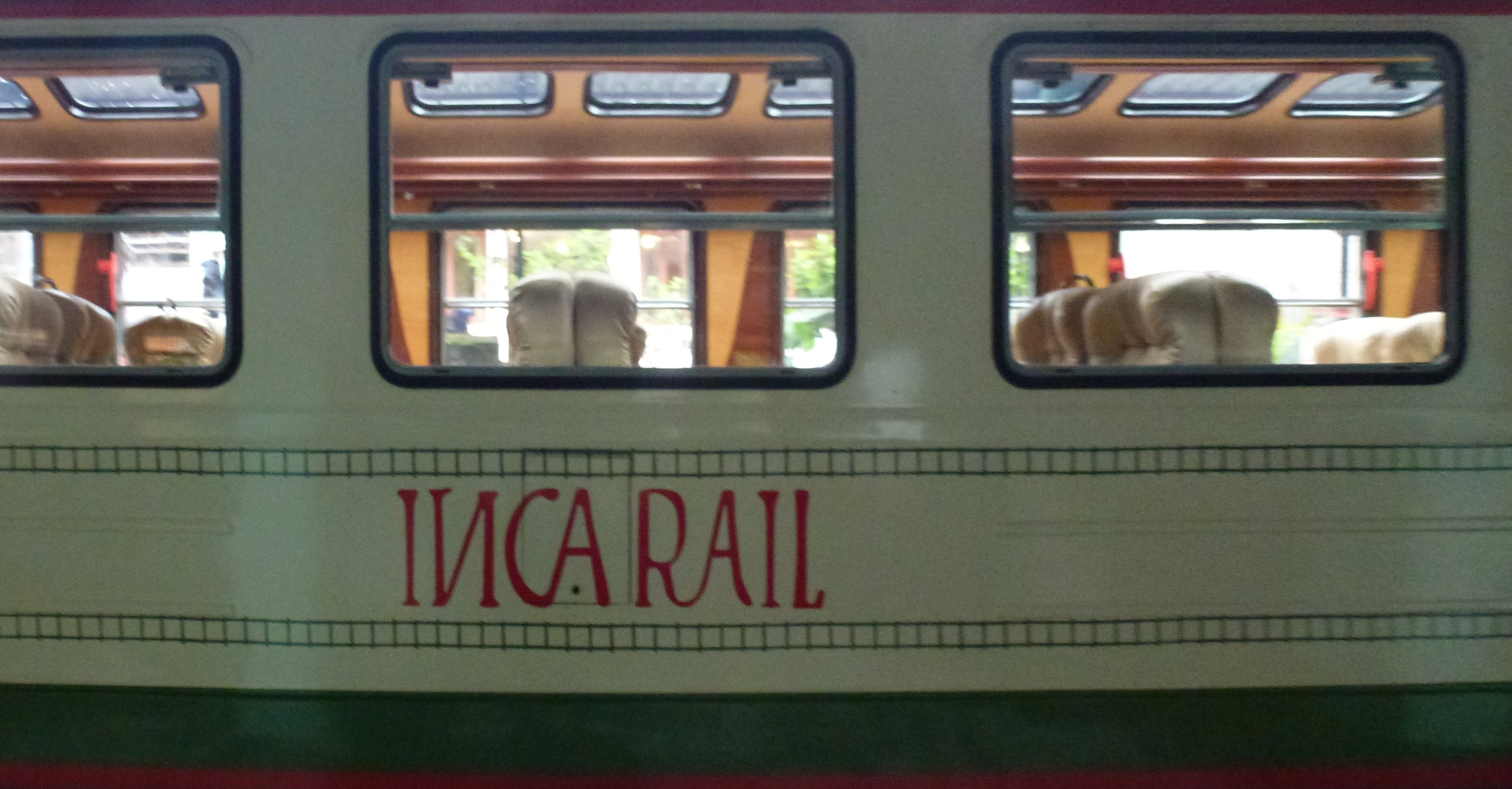 The side of an Inca Rail carriage at Ollantaytambo station, showing the tall windows and upholstered seats of the cabin.