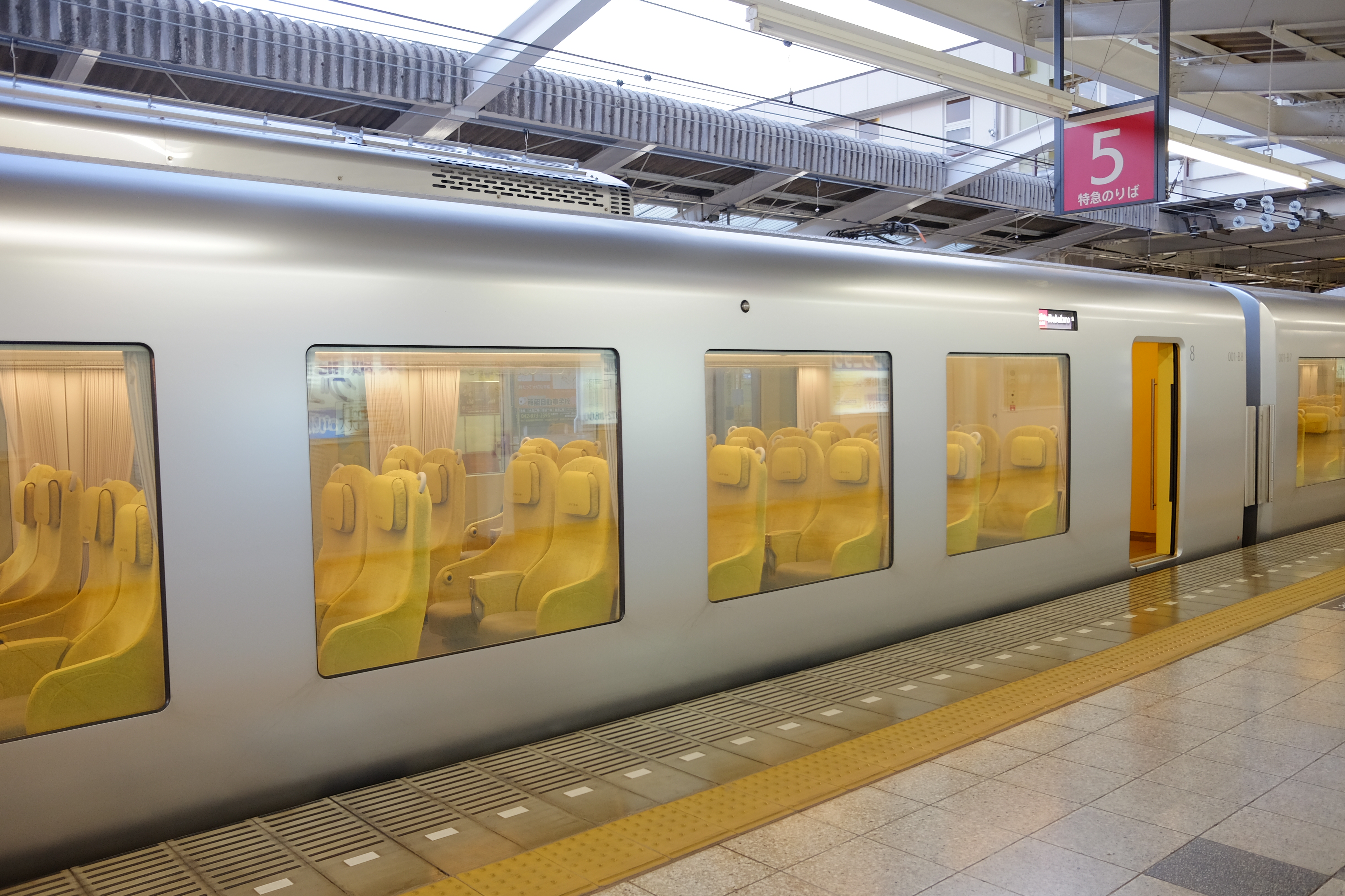 A Seibu 001 series Laview at Ikebukuro, its yellow seats visible through the floor-deep side windows.