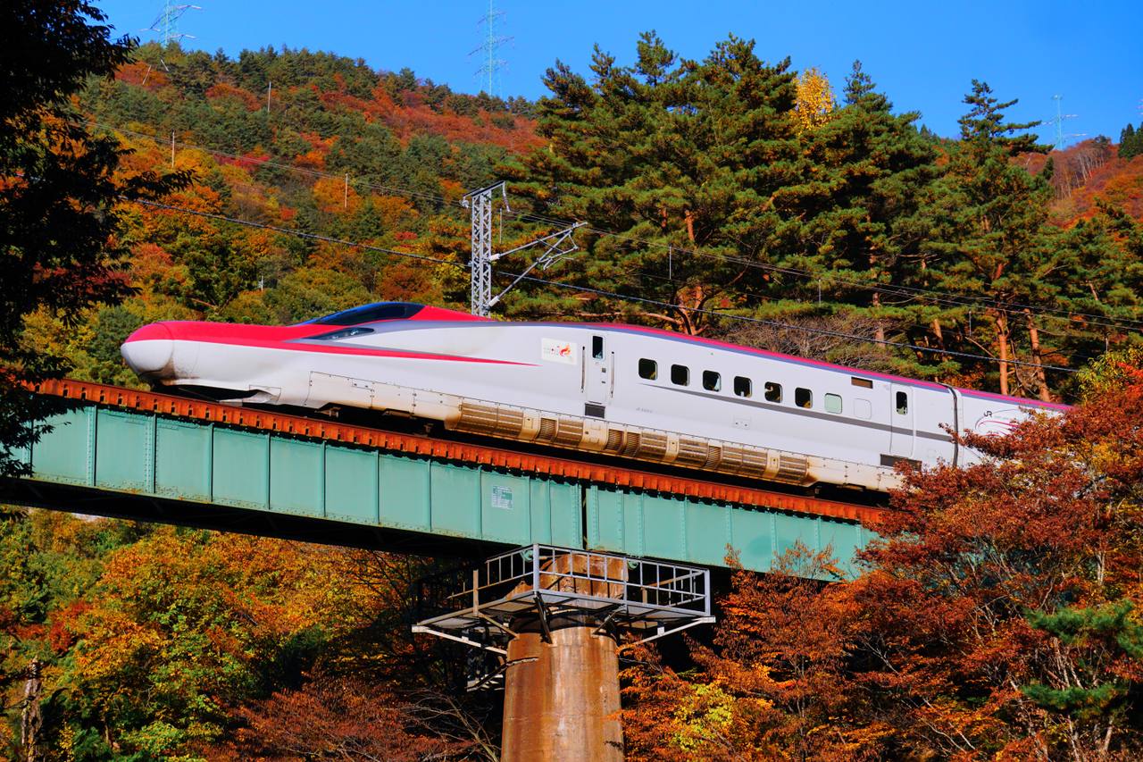 An E6 series Komachi Shinkansen crossing a bridge in autumn colour.