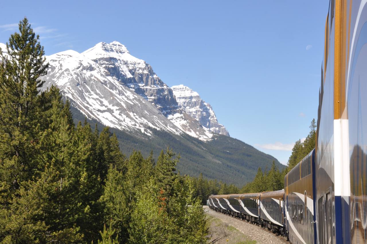 A Rocky Mountaineer train curving below the snow-capped Canadian Rockies.
