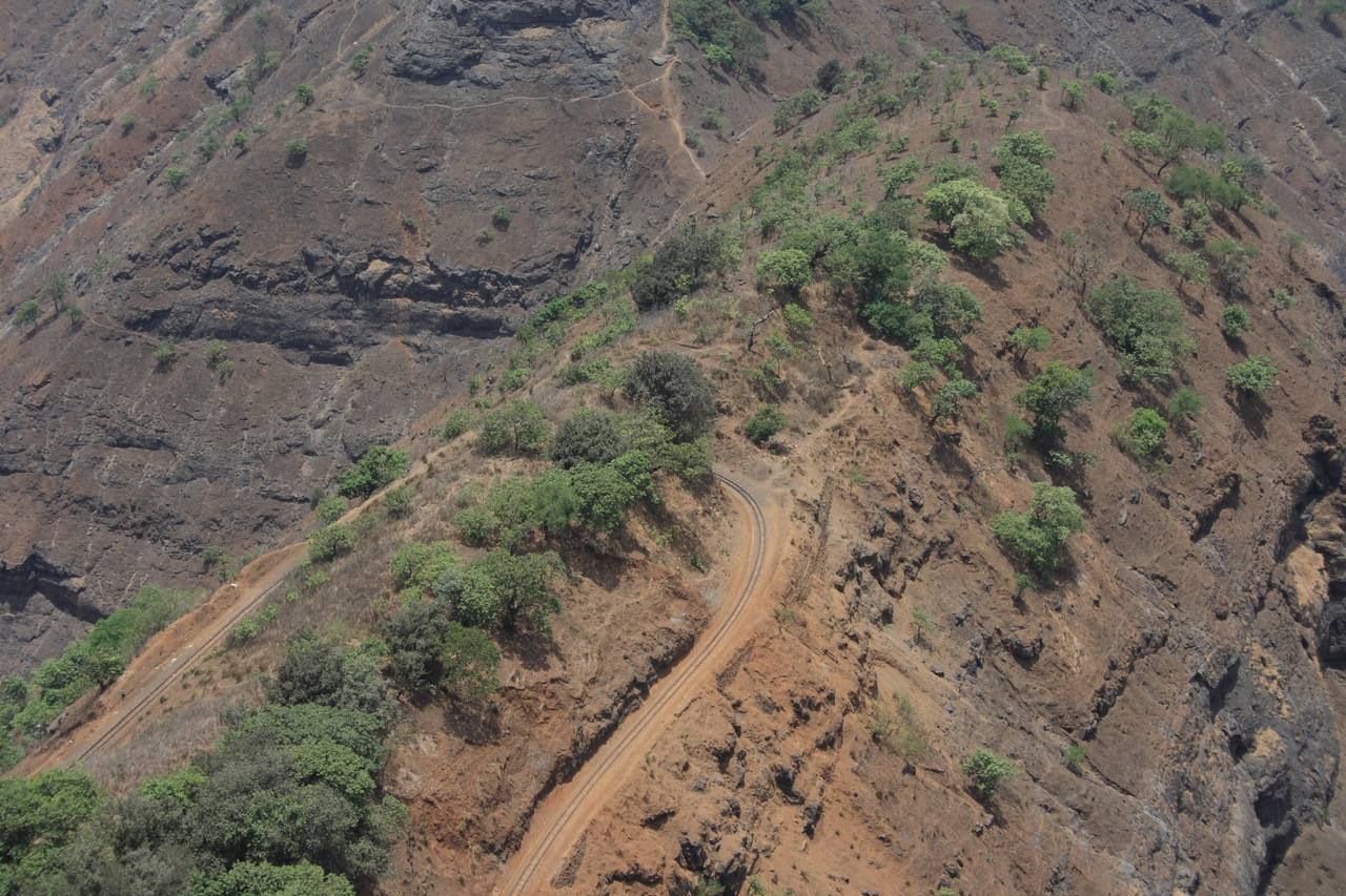 A Matheran Hill Railway train rounding a cliff-edge bend above the plains.