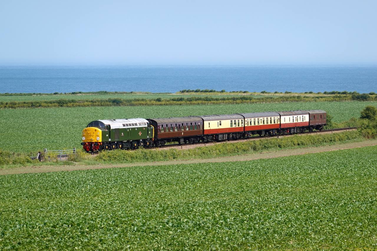 North Norfolk Railway passenger train crossing coastal fields near Weybourne.