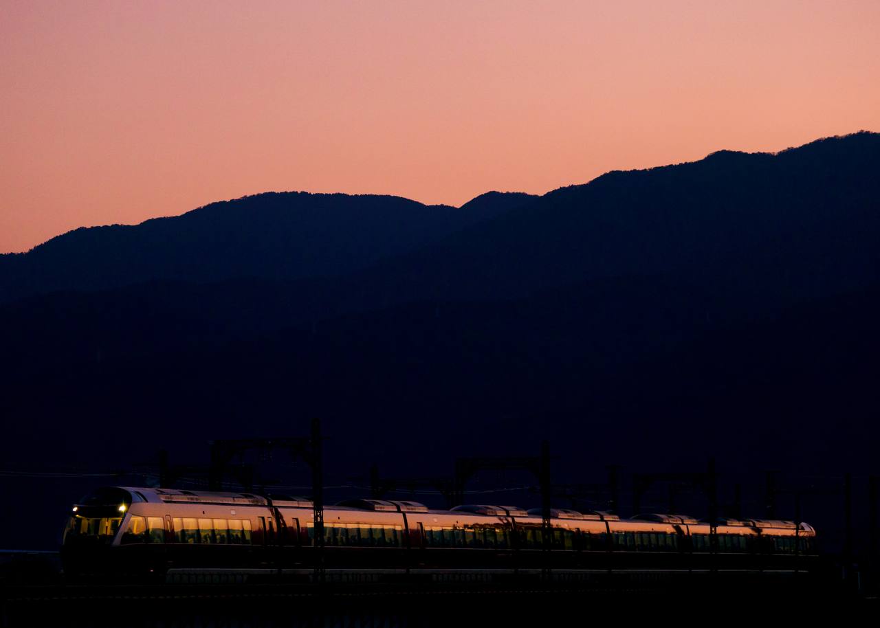 An Odakyu 70000 series GSE Romancecar crossing the Sakawa river bridge at dusk.