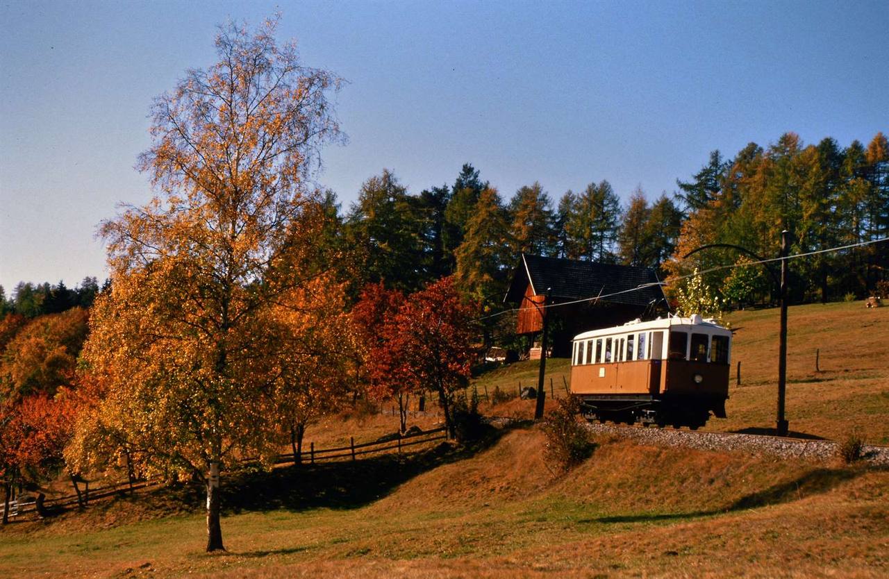 Heritage Ritten Railway railcar crossing autumnal South Tyrol countryside.