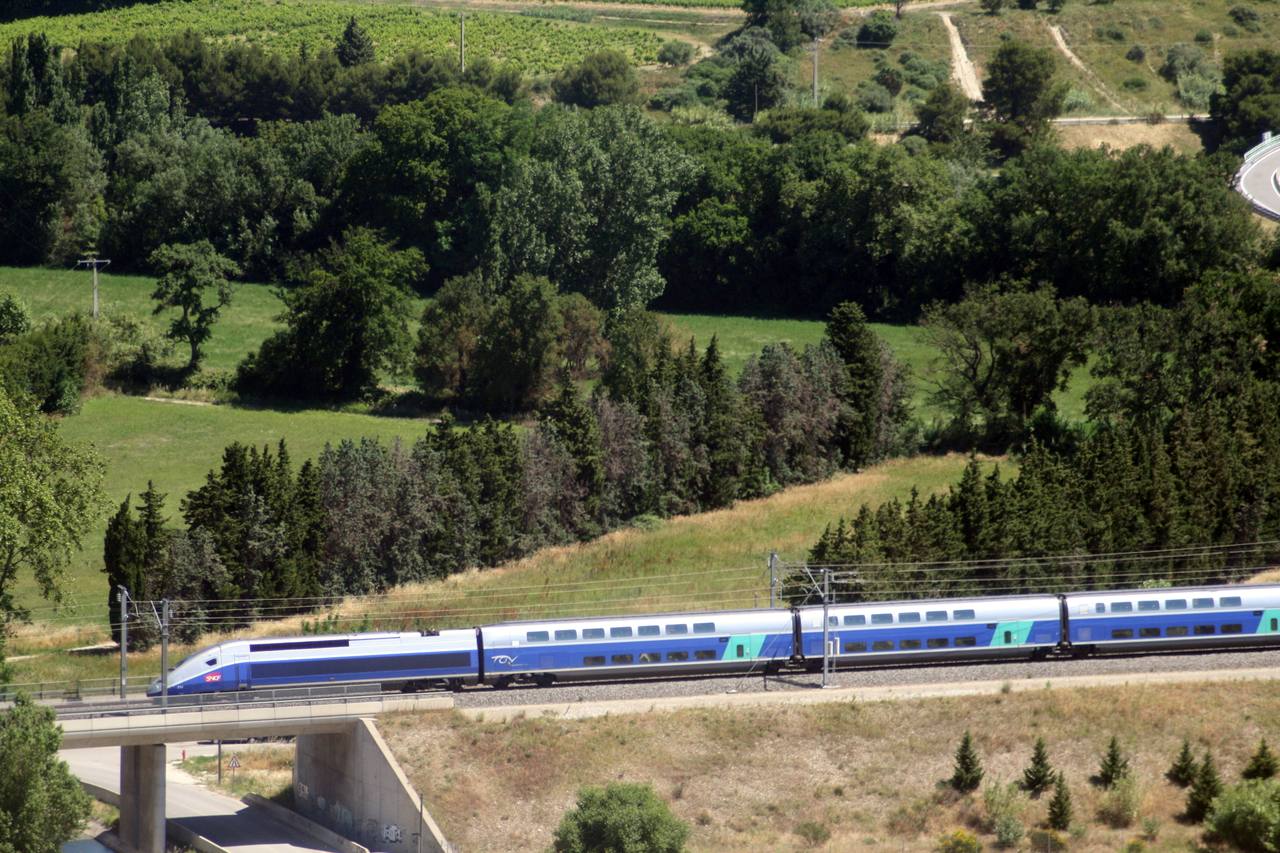 A TGV Duplex runs at speed across the sunlit Provencal landscape on the LGV Mediterranee.