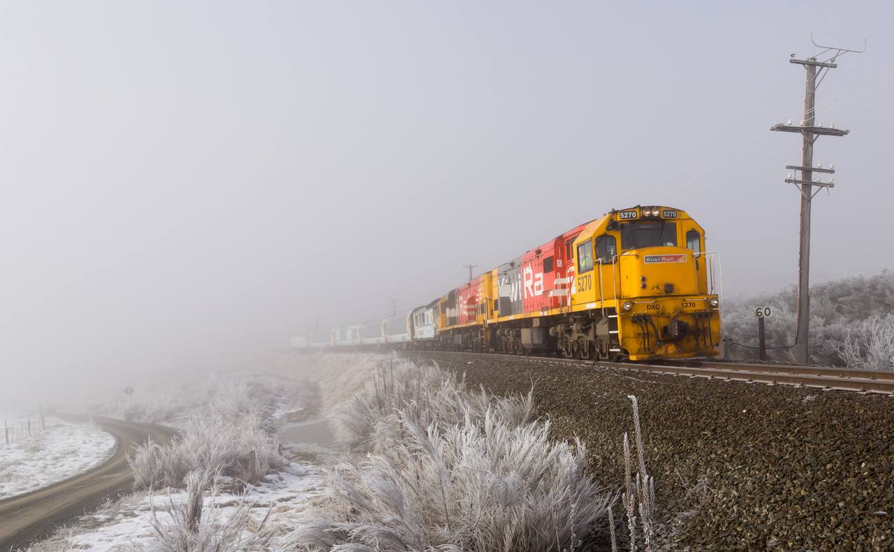 A TranzAlpine service crosses the frosted Canterbury landscape behind its locomotives.