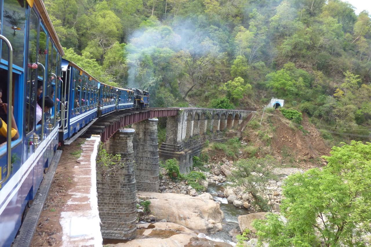 Nilgiri Mountain Railway train crossing a stone bridge in Tamil Nadu.